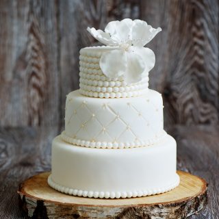 Wedding cake covered with white fondant, decorated with beads and hand-made flower on top