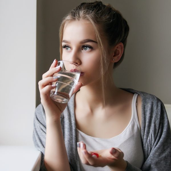 Jeune femme tenant des gélules et buvant un verre d'eau