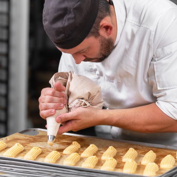 Pâtissier en train de confectionner des éclairs avec une poche à douille