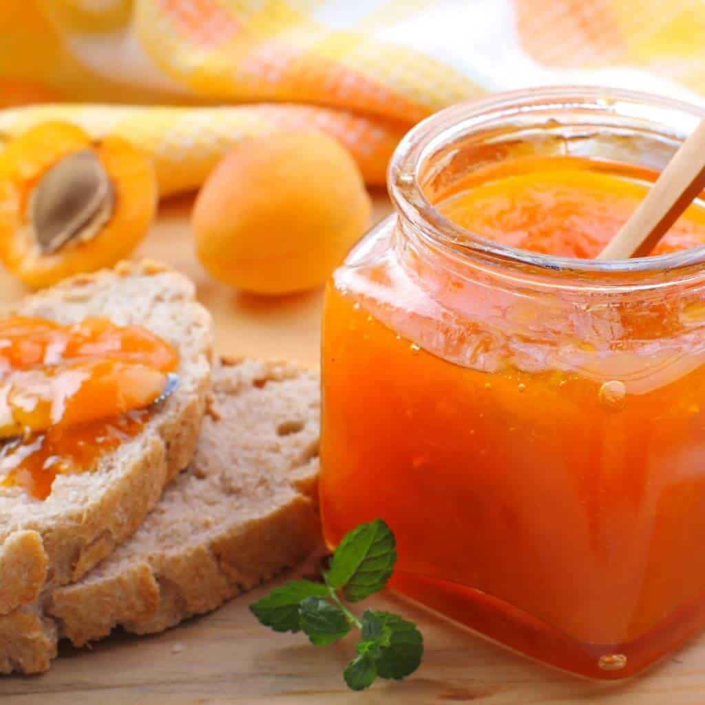 Apricot jam in a jar with bread on the side and fresh apricots in the background