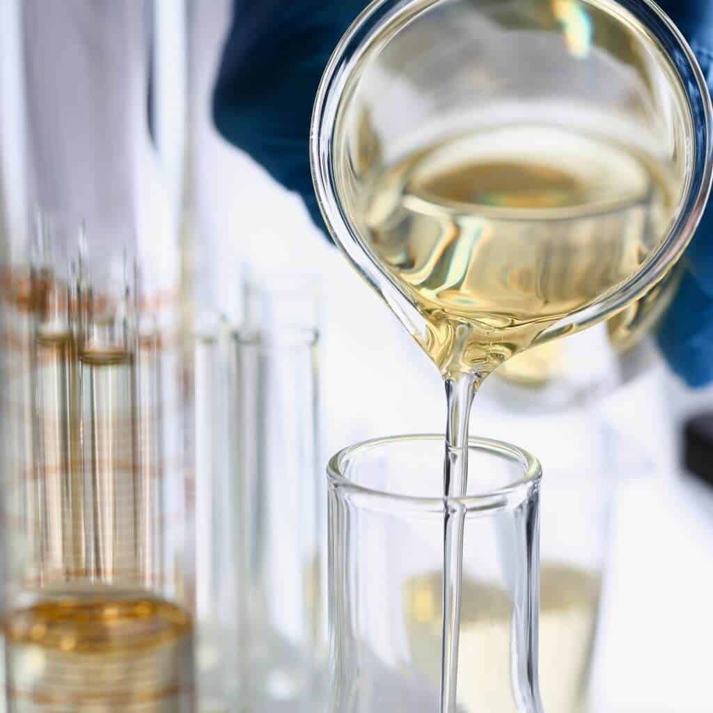 Liquid sugar is poured from a beaker into a test tube, with a laboratory environment in the background.